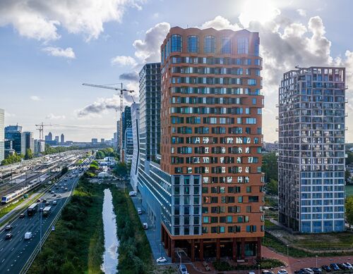 Buitenaanzicht van het project The Pulse in Amsterdam met moderne hoogbouw en stedelijke vervoersinfrastructuur.