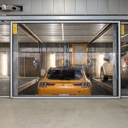 De afbeelding toont een gele sportwagen in een parkeersysteem binnen een moderne ondergrondse parkeergarage.